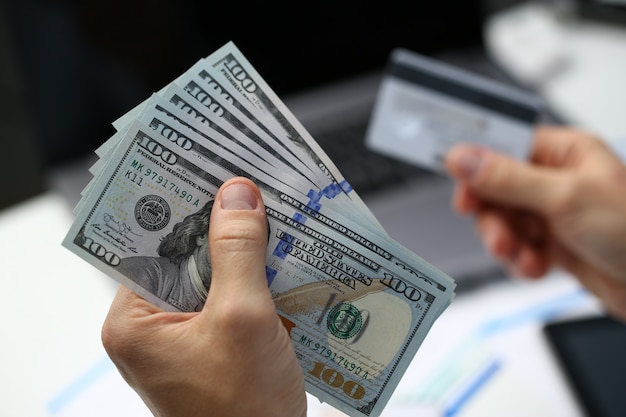 Male hand holds dollar banknotes and plastic bank card in hands closeup. Cash out money earned on web to your account cashes through payment terminal pay per click concept.