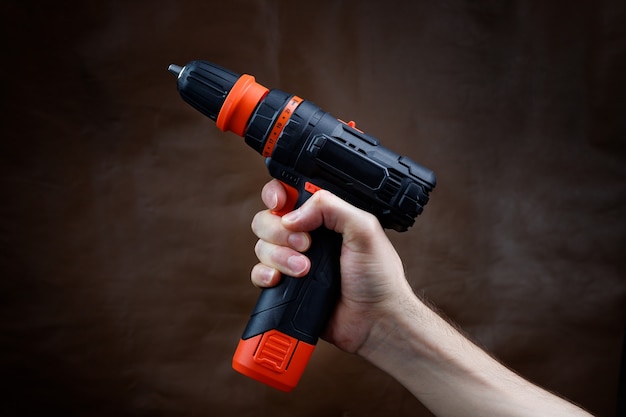 The male hand holds an electric screwdriver on a dark brown background