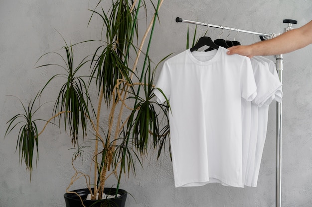 Male hand holds hanger with blank white t-shirt, close up