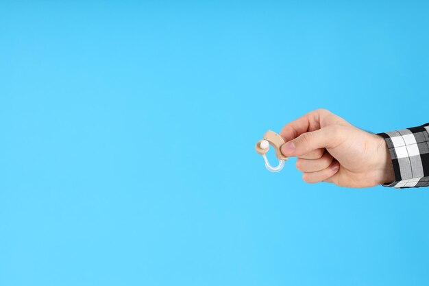 Male hand holds hearing aid on blue background