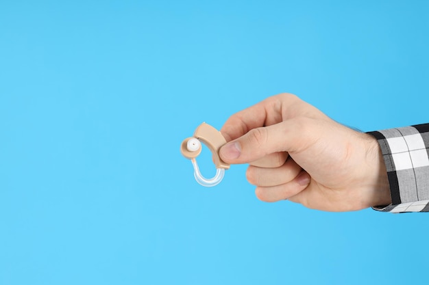 Male hand holds hearing aid on blue background