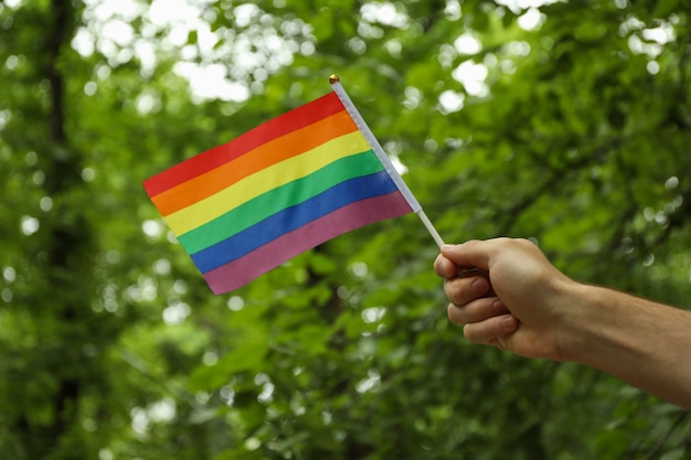 Male hand holds LGBT flag outdoor against greenery