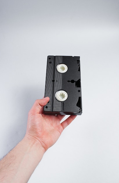 Male hand holds retro video cassette on gray surface.