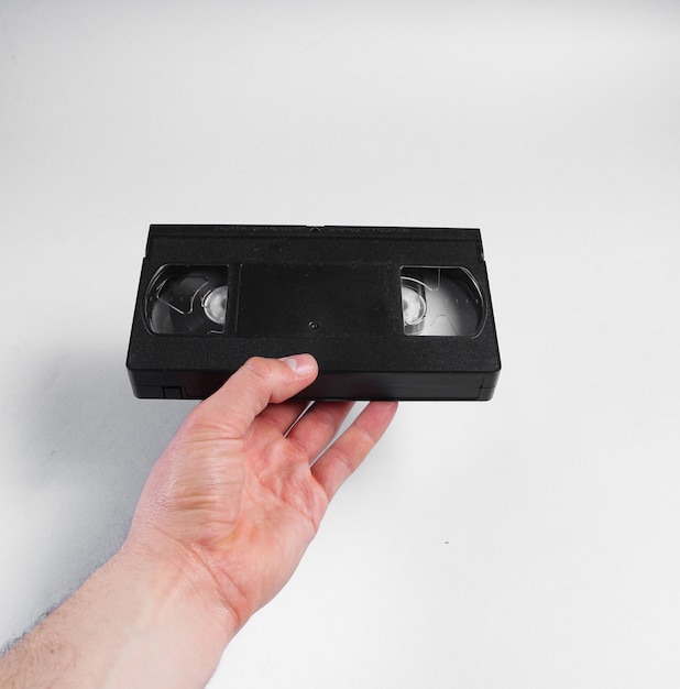 Male hand holds retro video cassette on gray surface.