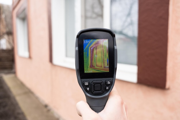 Photo a male hand holds a thermal imager at the window of a house. search for heat loss in private houses.