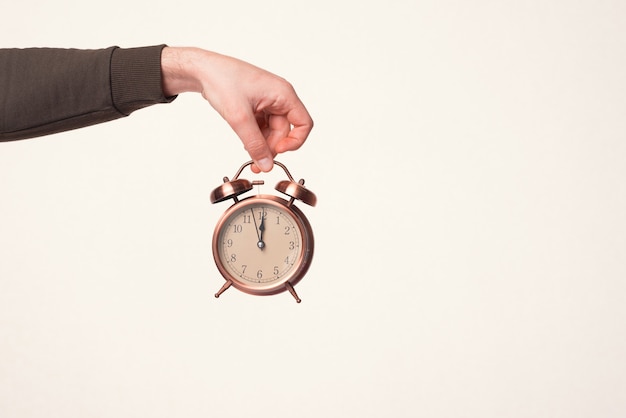 Male hand is holding an alarm clock over warm white background.