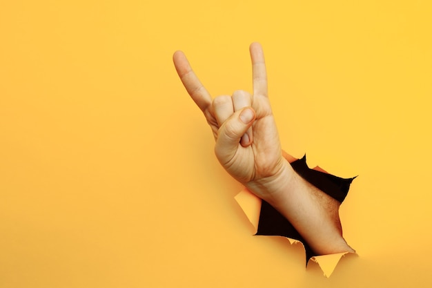 Male hand making a rock and roll gesture party goat on a yellow background