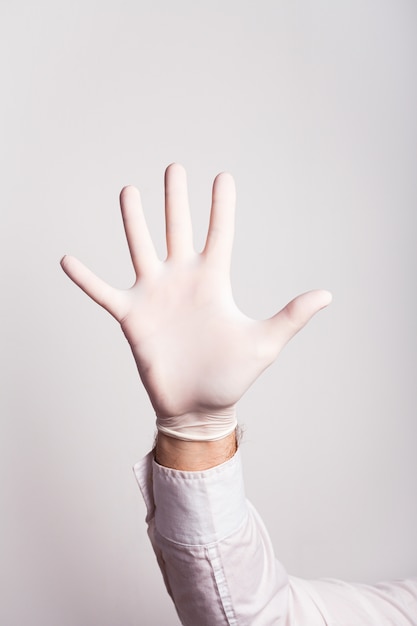 A male hand in a medical glove shows five fingers on a white wall