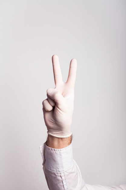 Male hand in a medical glove shows two fingers on a white wall