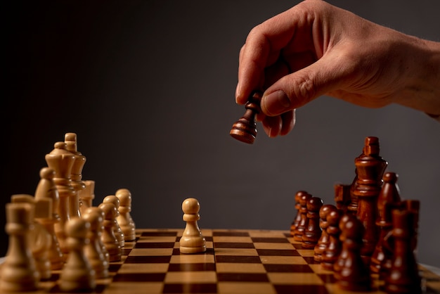 Male hand moving pawn on chess board, starting game. Making business decision concept.