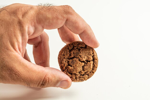 Foto mano maschile che raccoglie un biscotto al cioccolato su sfondo bianco