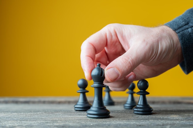 Male hand positioning black chess figure in front of the others in a conceptual image of leadership and power