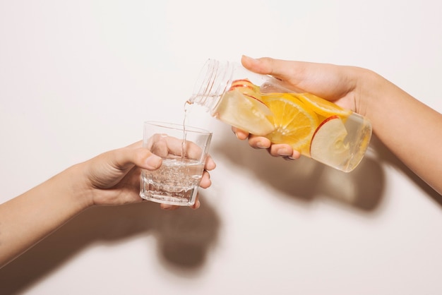 Male hand pours detox water into glass. Detox water, fitness, healthy nutrition diet concept. Fresh lemon cucumber mint detox drink in glass on white wooden table