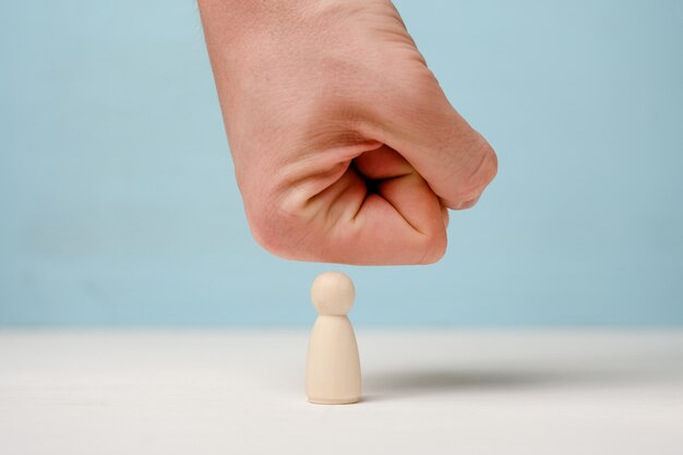 Male hand presses on wooden figure on blue background.