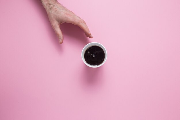 A male hand reaches for a glass with a coffee on a pink