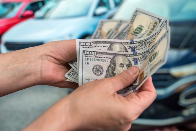 Male hand showing a dollar for buying a car in the autohouse. finance