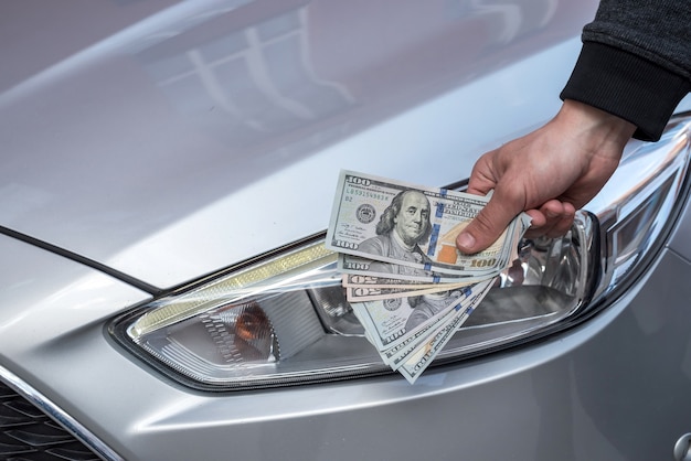 Male hand showing a dollar for buying a car in the autohouse. finance