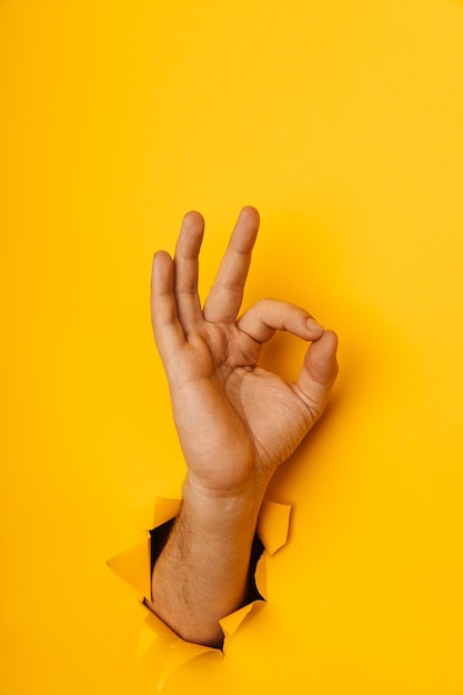 Male hand showing ok through a hole in yellow background vertical image