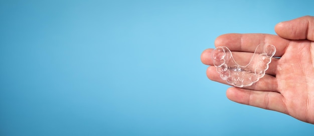 Male hand showing transparent aligner on the blue background