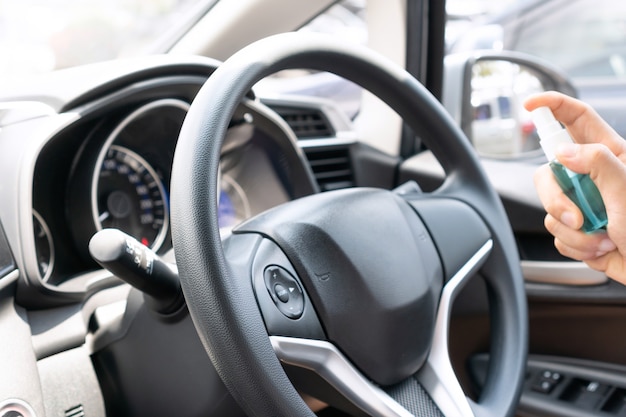 Male hand spraying alcohol to car steering wheel for disinfecting.