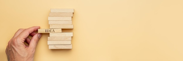 Male hand stacking wooden pegs with Idea sign one one of them in axAconceptual image Over yellow background