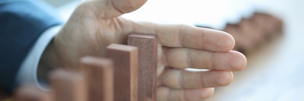 Male hand stopping falling of wooden blocks in line closeup