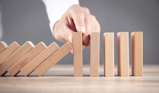 Male hand stopping wooden domino. Business. Crisis. Risk