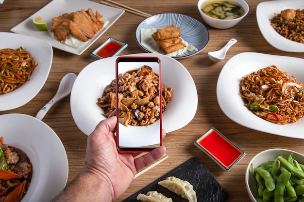 La mano maschile scatta una foto con lo smartphone del cibo sul tavolo del ristorante orientale.