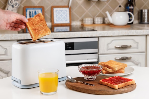 Male hand takes the toaster bread out of the white toaster Glass of orange juice