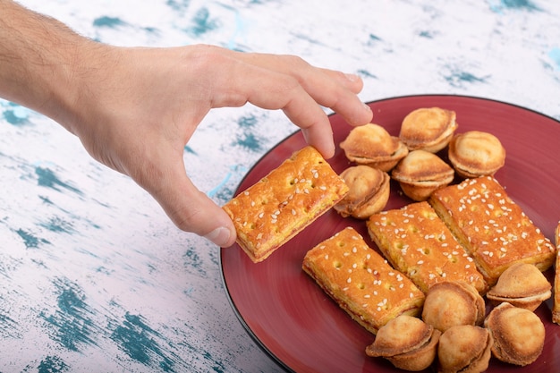 Мужская рука берет сладкий крекер возле небольшого печенья в виде грецких орехов, помещенных в тарелку.