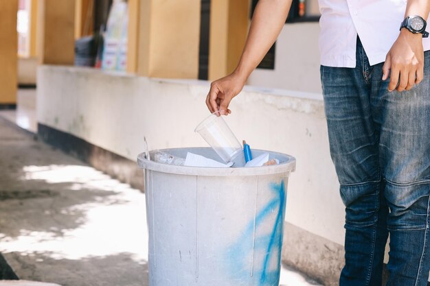 Foto mano maschile getta una tazza di plastica nel cestino della spazzatura concetto di conservazione ambientale