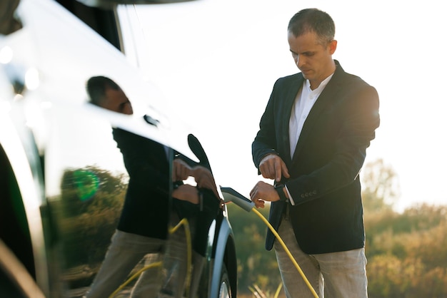 Male hand unplugs power connector into ev car and charges\
batteries uses smart watch to disconnect