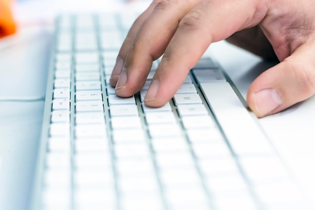 Foto un uomo passa la mano sulla tastiera bianca di un computer prima di digitare la tecnologia del lavoro e dell'occupazione