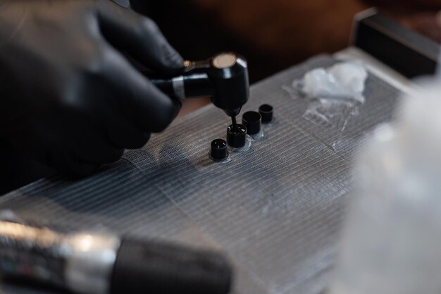 Foto mano maschile con guanto nero mescolare la vernice con un mixer. il tatuatore prepara la vernice prima del tatuaggio