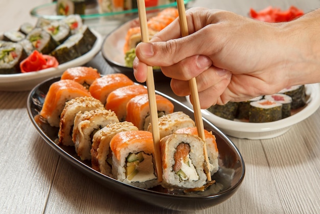 Male hand with chopsticks holding Uramaki roll with Conger and different sushi rolls with seafood