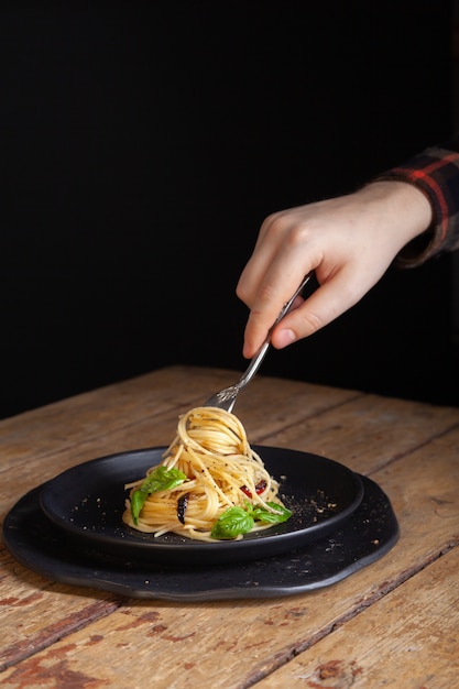 male hand with italian spaghetti, fork serving on black dishes