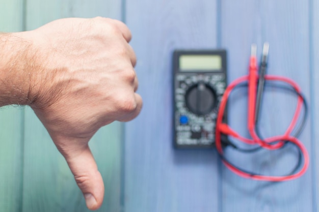 Male hand with a negative gesture on the background of an electronic multimeter to measure current