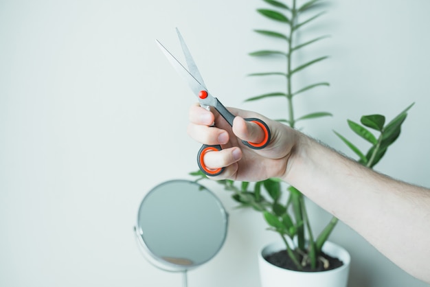 Male hand with scissors opposite the mirror. Stay home.