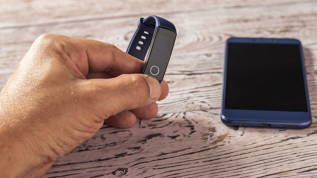 Male hand with smart bracelet and a smartphone on a wooden table. Accessories to control sports. Sports style.