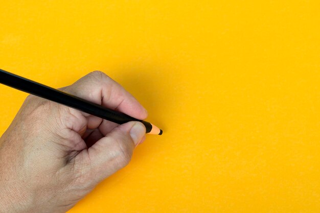 Male hand writes in black pencil on a yellow background copy space teaching concept