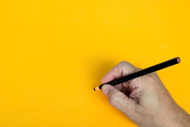 Foto mano maschile scrive a matita nera su sfondo giallo copia spazio concetto di insegnamento