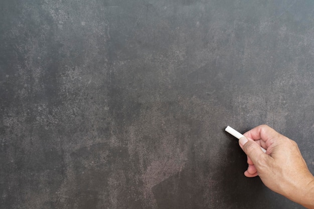 Photo male hand writes in white chalk pencil on a chalkboard background copy space teaching concept