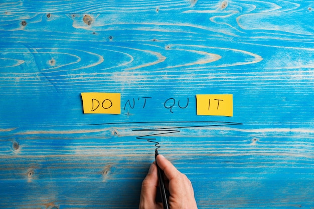 Male hand writing a Dont quit Do it sign on bright yellow papers