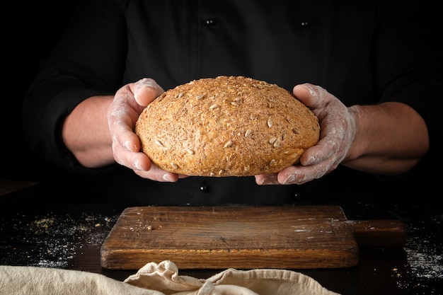 Male hands are holding brown baked rye bread 