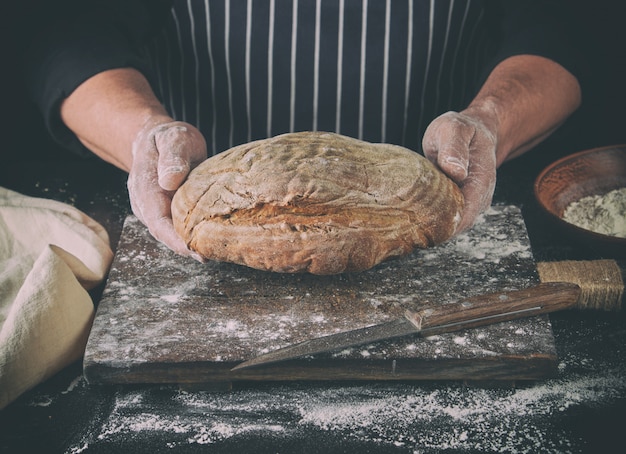 Male hands are holding brown baked rye bread