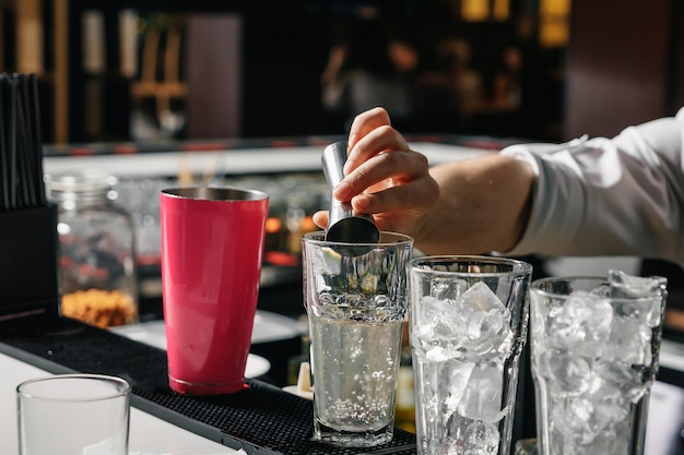 Male hands of the bartender, makes a cocktail on the bar, glasses with ice.