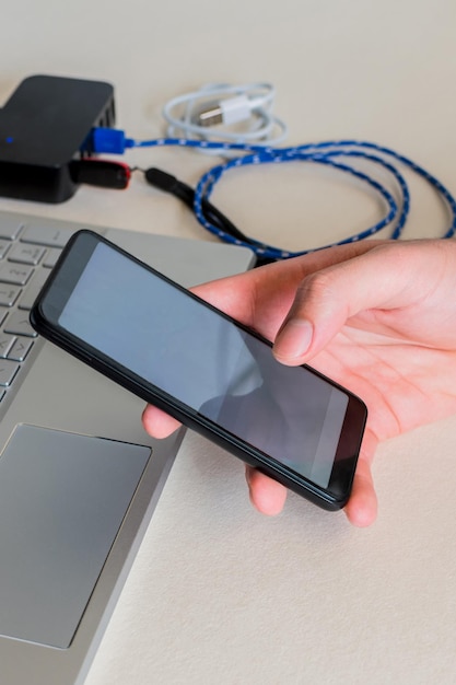 Male hands checking cell phone next to laptop on desk Selective focus