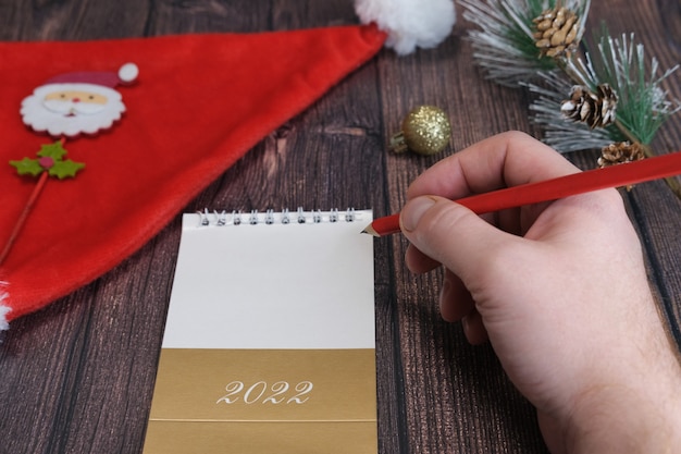 남성 손 클로즈업입니다. 한 남자가 산타클로스에게 편지를 씁니다. 2022년 크리스마스, 새해에 대한 개념입니다.