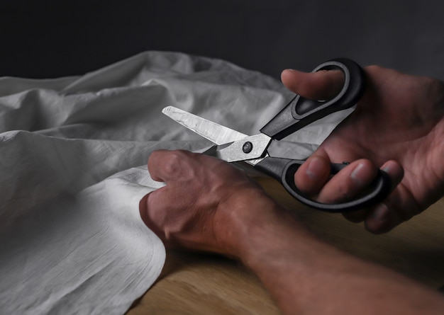 Male hands closeup cutting beige cotton or linen cloth with sewing scissors.