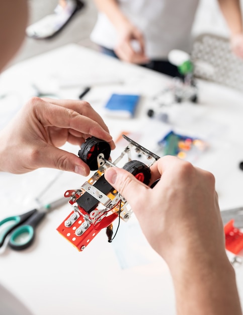 Male hands constructing robot cars at the workshop